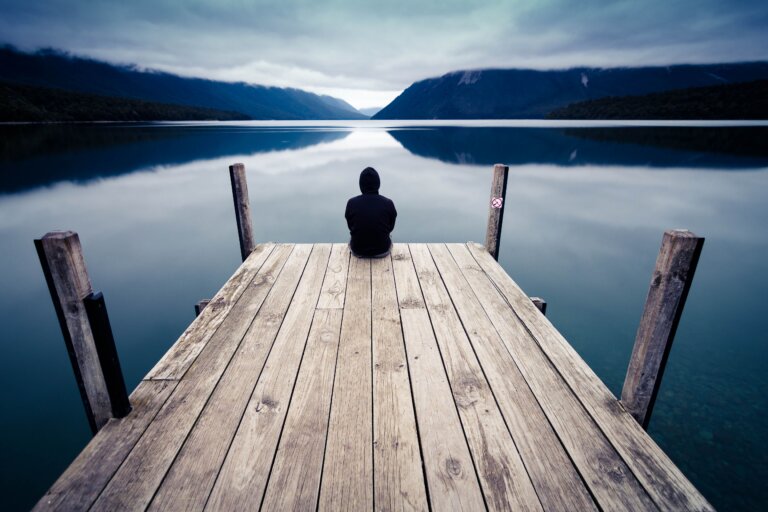 Man sitting alone beside a peaceful river in quiet reflection