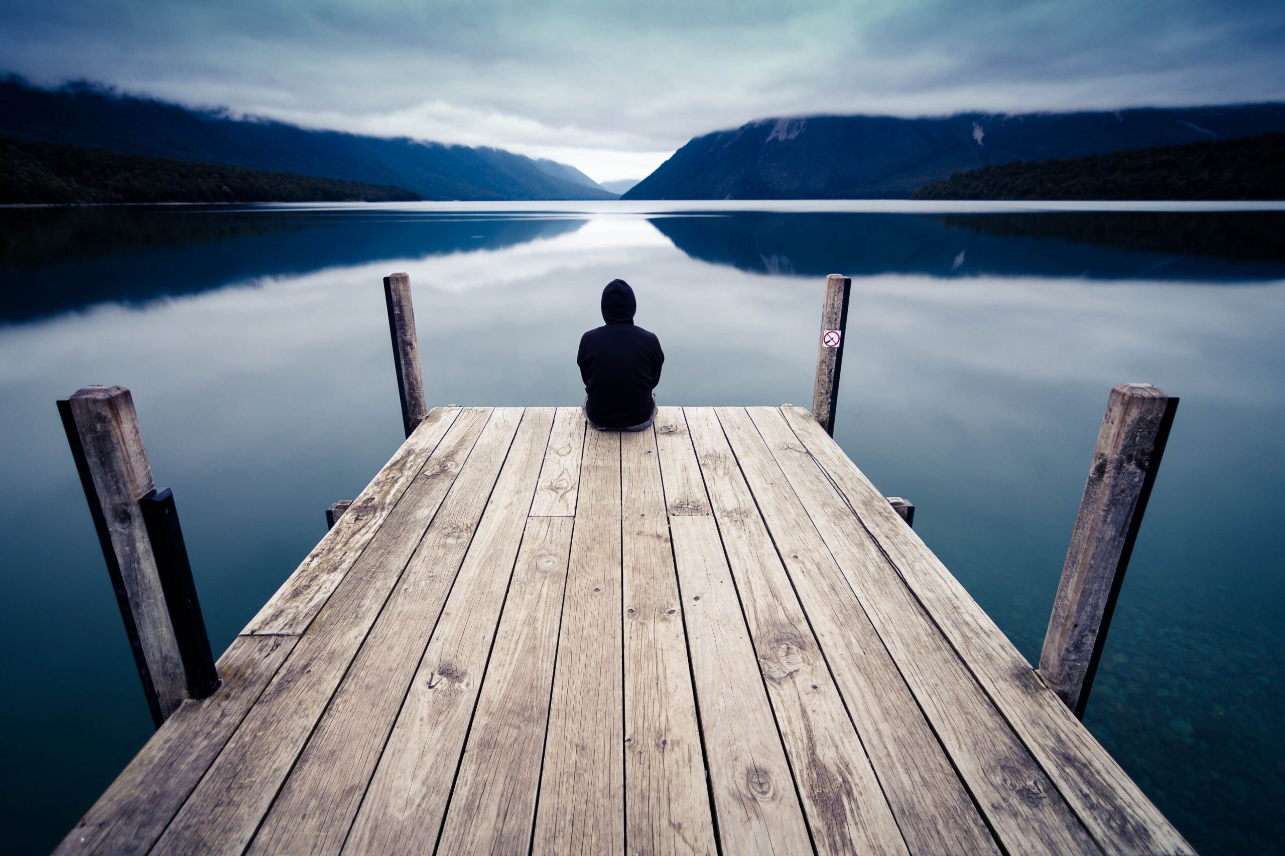 Man sitting alone beside a peaceful river in quiet reflection