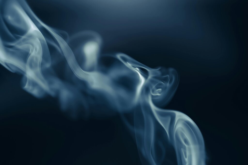 Thick white vapor cloud rising from a person exhaling a vape, with a blurred background vaping