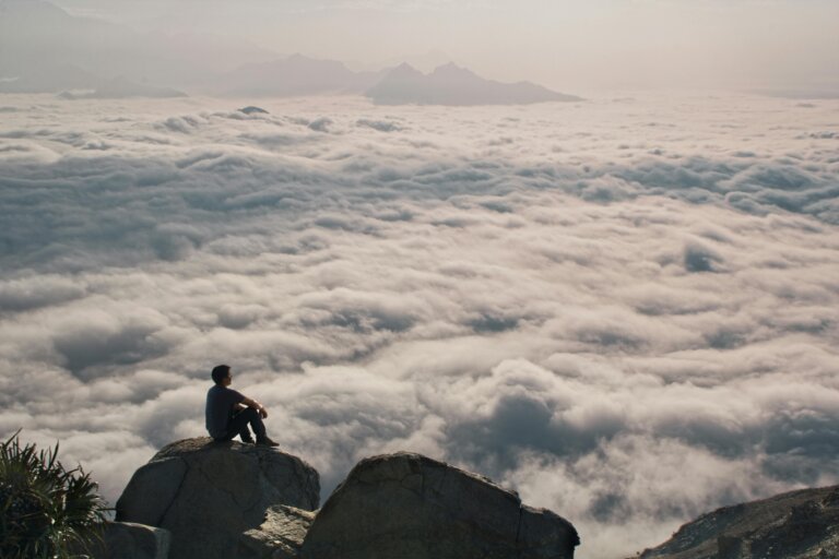 A person sitting peacefully on a mountain peak, overlooking a vast landscape, radiating calm and clarity. general anxiety