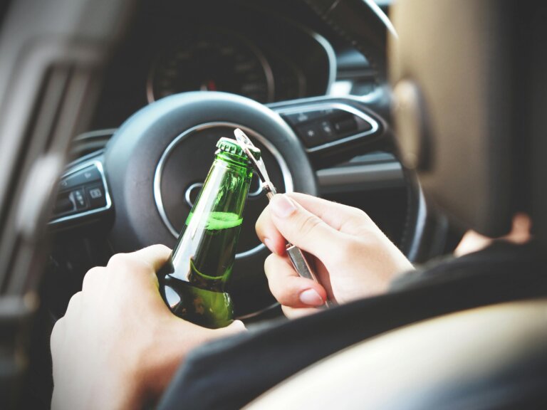 Man sitting in a car opening a bottle of alcohol, depicting alcohol addiction